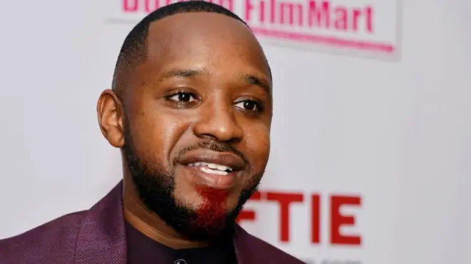 Une photo de Boniface Mwangi qui parle. Il porte une veste sombre et une chemise noire sans col.