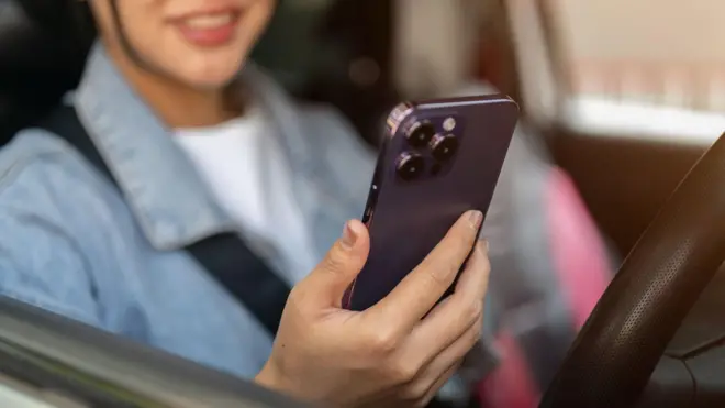 A close-up of a positive Asian woman using her smartphone while stopped at traffic in the city. 