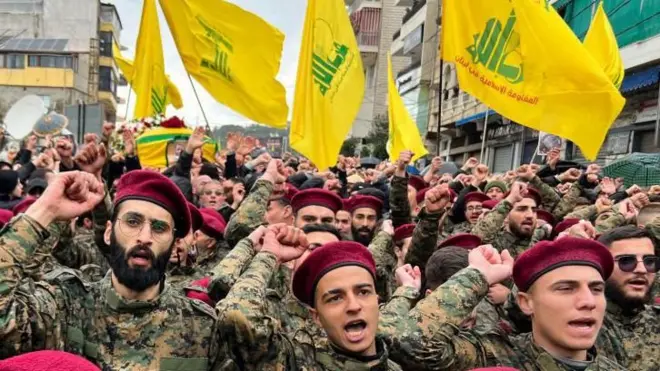 Des membres du Hezbollah en uniforme militaire défilent avec les drapeaux du groupe en arrière-plan.