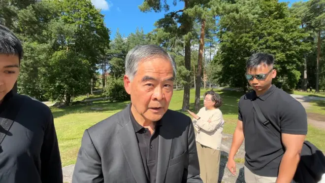 芬蘭赫爾辛基西貝柳斯公園內，被指恐嚇法輪功學員，身穿黑色西裝的梁振英（中）望向鏡頭（法輪大法信息中心發放影片截屏13/8/2025）