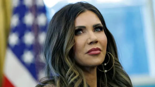 クリスティ・ノーム国土安全保障長官が口を閉じ、前方を見ている。後ろには星条旗が置かれている