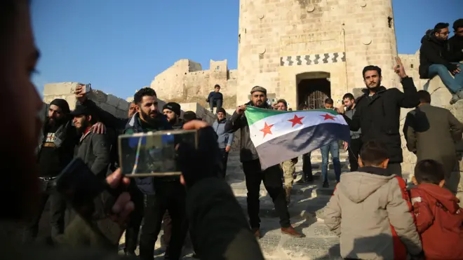 يحمل أنصار المعارضة العلم السوري للمعارضة بينما يتجمع الناس على جانب قلعة حلب، في حلب، سوريا.