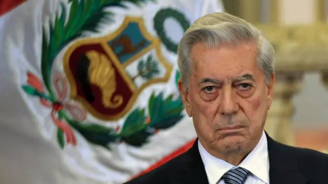 Mario Vargas Llosa serio frente a la bandera de Perú.