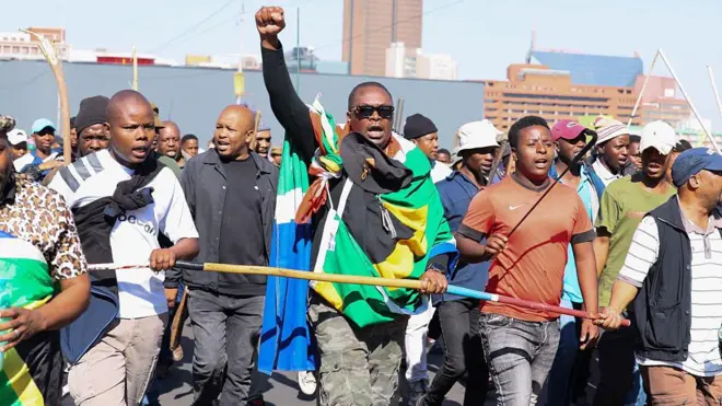Man hold im hand up during protest, oda men dey im side