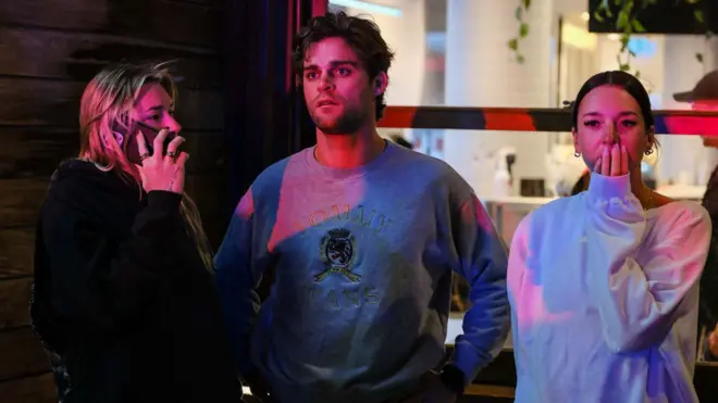 悉尼邦迪海灘外數名途人遠眺槍擊現場，一名女士（右）掩面神傷（14/12/2025）