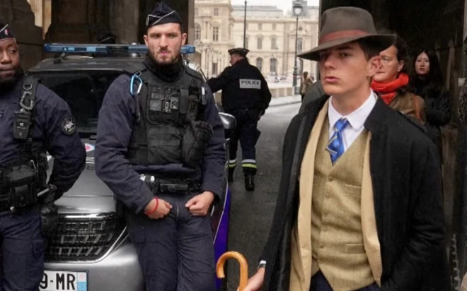 İki polisin yanında dedektif gibi giyinmiş, elinde şemsiye tutan bir genç