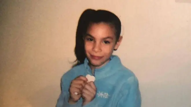 A young Delimar holds a heart shape in her hands 