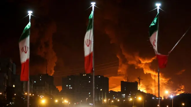 Bandeiras de Irã em frente a prédios em chamas