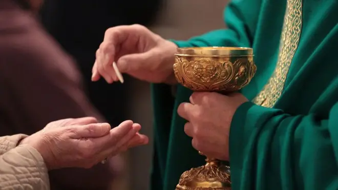 Close na mão de um padre entregando a óstia a uma pessoa