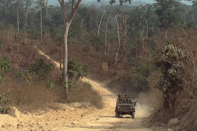 Une patrouille de l'armée guinéenne à la frontière entre la Guinée et le Libéria, des militaires armés dans un jeep qui roule sur un sentier poussièreux au milieu d'une forêt.