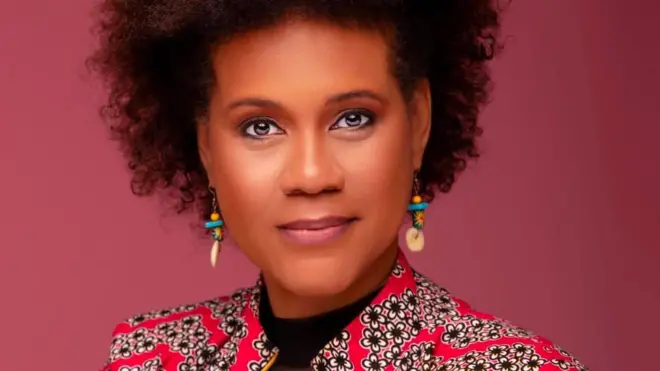 Ifoto ifatiwe hafi igaragaza Maria Sarungi Tsehai, yambaye ikoti ryo mu gitenge ririmo amabara atukura, inyuma ye hari ibara ry'iroza rijya kweruruka 