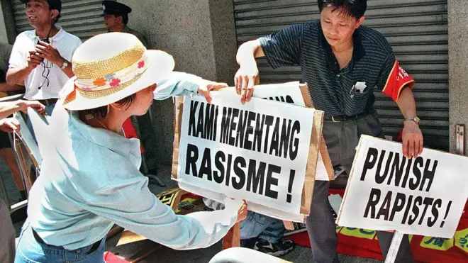 Plakat dengan tulisan "Kami menentang rasisme!" dan "Menghukum para pemerkosa!", di depan Konsulat Indonesia di Hong Kong, 26 Juli 1998.