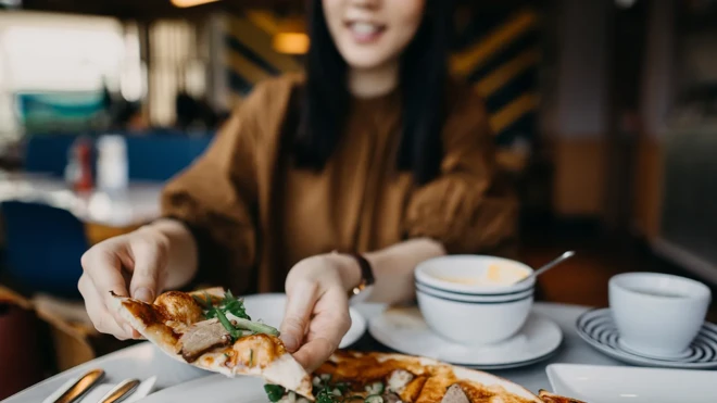 دختری یک برش پیتزا از بشقاب برمی‌دارد