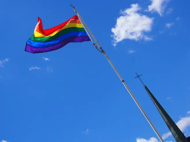 A Rainbow flag flies near a cross belonging to a Catholic church