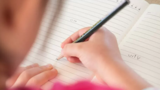 صورة تظهر جانب من فتاة صغيرة تمسك قلماً وتكتب 