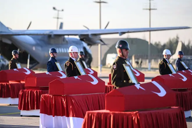 Ankara'daki Mürted Hava Üssü'nde düzenlenen törende bayrağa sarılı tabutlar ve başlarında askerler görünüyor, arka planda bir uçak var