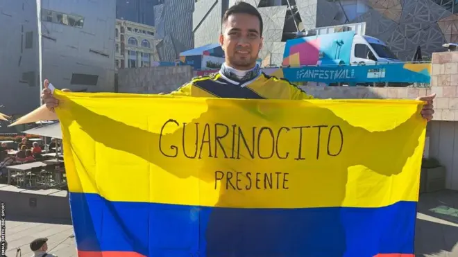 Kevin con una bandera de Colombia que dice "Guarinocito presente"