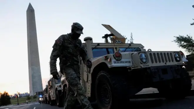 A soldier standing near the Washington Monument obelisk. He stands next to a military Humvee