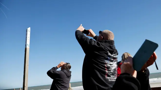 Homens apontando celulares e binóculos para o céu