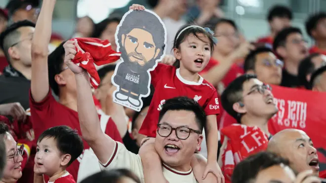 一名男子背著女孩，手舉支持利物浦隊的紙牌和圍巾