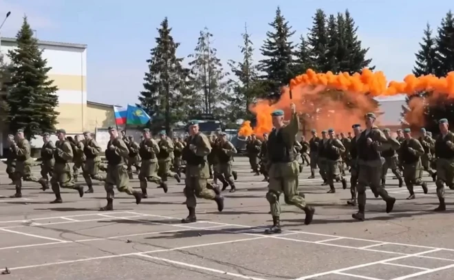 Des hommes en uniforme courent. Certains lèvent un fumigène qui dégage de la fumée orange