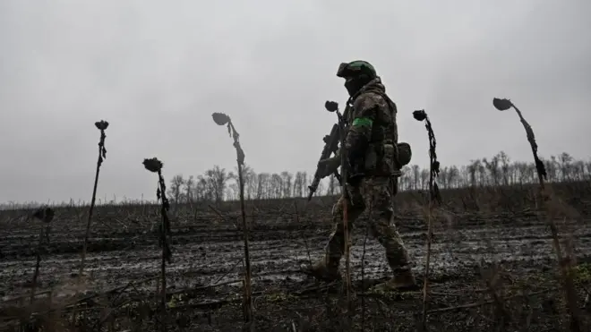 Украинский военный в форме и с автоматом идет по полю.