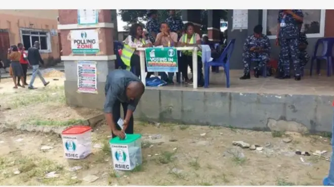 Aworan yii ṣafihan ọkunrin kan to bẹrẹ to si n sọ iwe idibo rẹ sinu apoti idibo, awọn eleto idibo naa wa lapa oke, wọn jokoo, wọn kawọ le tabili kan. Awọn agbofinro wa nibẹ pẹlu, bẹẹ si ni awọn to n fẹsẹ rin kọja tun wa ninu aworan idibo ijọba ibilẹ to waye nipinlẹ Rivers ni Satide, ọgbọnjọ oṣu Kẹjọ ọdun 2025.