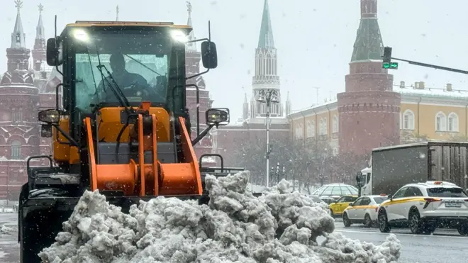 Трактор сгребает кучу снега у стен московского Кремля