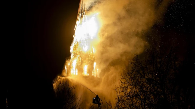 Kilisenin kulesi alevler içinde, bir itfaiye eri gece karanlığında su sıkıyor.