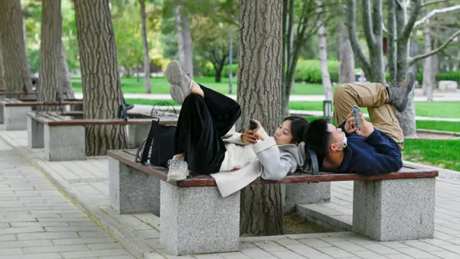 Um casal chinês usando seus respectivos celulares enquanto estão deitados em um banco em um parque em Pequim em 21 de abril de 2021