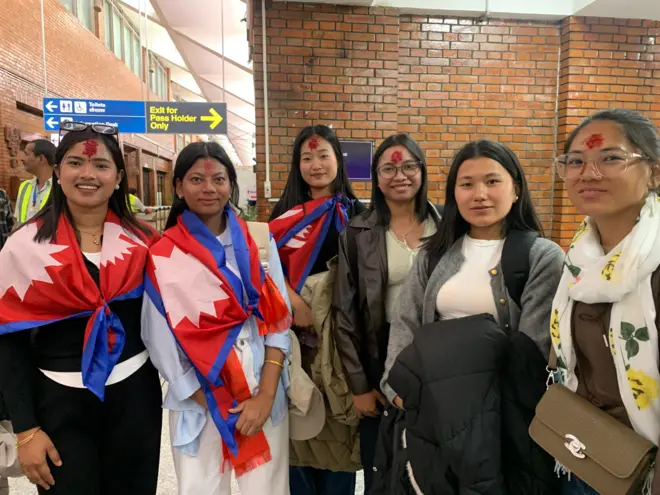 अध्ययनका लागि जापान जान लागेका ६ जना नेपाली किशोरी त्रिभुवन अन्तर्राष्ट्रिय विमानस्थलमा। उनीहरू मध्ये तीनले घाँटीमा नेपालको चन्द्र र सूर्य अङ्कित झन्डा बेरेका छन्।