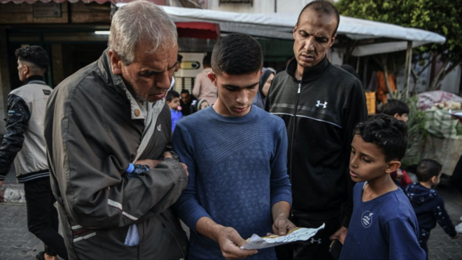 Dois homens e dois meninos em uma rua em Gaza olham para um folheto com alerta de evacuao emitido pelas FDI