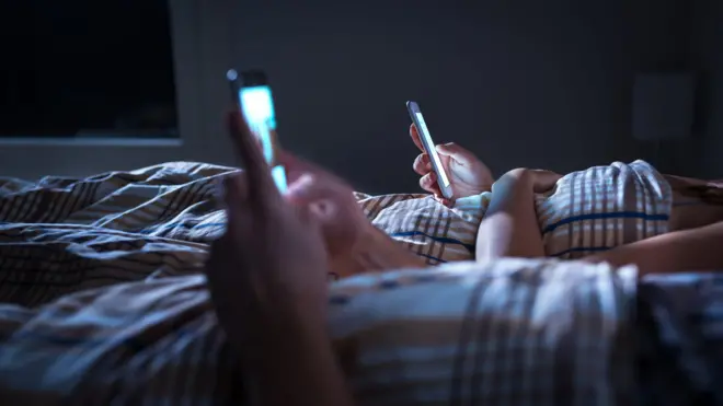 Duas pessoas deitadas na cama usando celulares