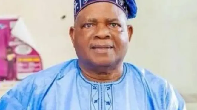 Kola Oyewo wọ aṣọ aláwọ̀ búlúù àti fìlà aláwọ̀ kan náà