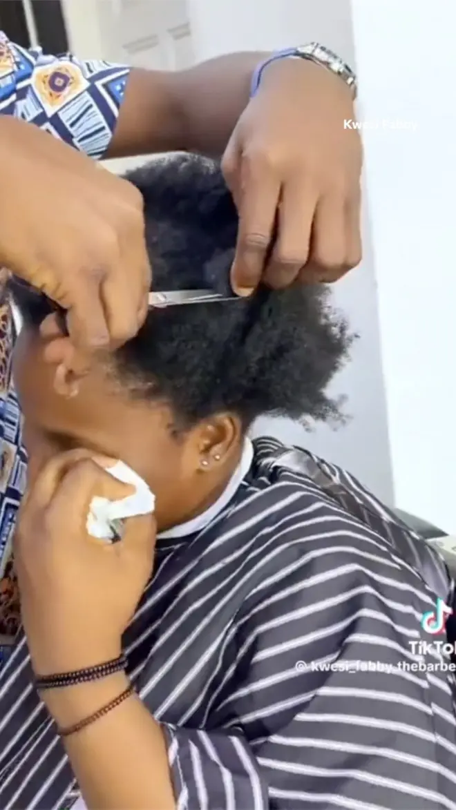 A girl cries and cleans her tears as her hair is being cut with scissors 