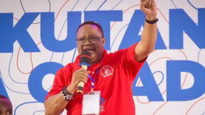 Umunyapolitike wo muri Tanzania Tundu Lissu arimo kuvugira mu ndangururamajwi. Yambaye umupira w'amaboko magufi w'umutuku, yazamuye igipfunsi. 