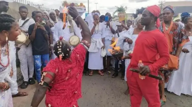 Awọn Onisango wọ asọ pupa, ru ina sori, ọkunrin kan to di irun sori n da ina si ẹnu, nigba ti awọn to wọ asọ funfun n woran