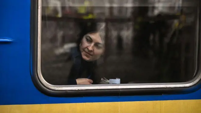 жінка в поїзді виглядає з вікна за склом - поїзд синьо-жовтий