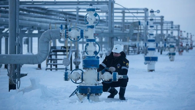 مردی در حال کار روی بخشی از تاسیسات گاز و نفت، فضای کار از برف سفیدپوش شده است