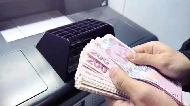 Bir ATM'nin önünde para sayan bir kişinin elleri.