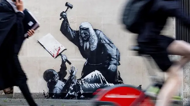 王立裁判所の壁に描かれたバンクシーの壁画の前を歩く法曹関係者