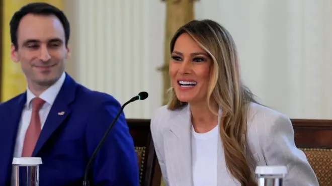 Melania Trump, dressed in a white jacket, speaking at a microphone at a table in the East Room of the White House on 4 September.