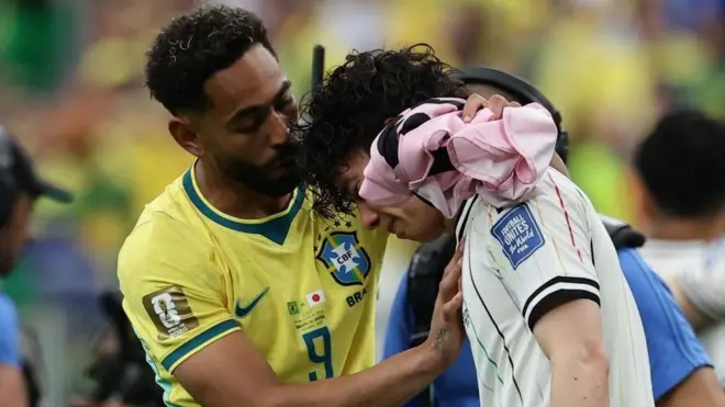 白色ユニホームの選手の胸に黄色ユニホームの選手が右手を当て、左手を頭の後ろに回している