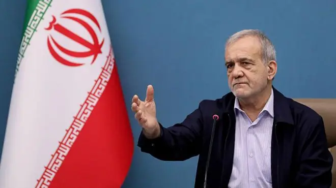 El presidente Pezeshkian, sentado con el brazo izquierdo alzado junto a una bandera de Irán.