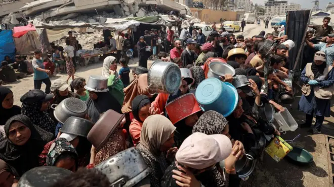 Grupa ljudi sa praznim šerpama čeka da primi humanitarnu pomoć