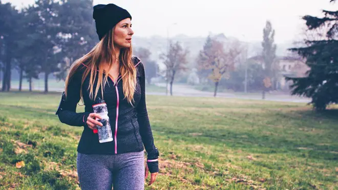 Mulher caminhando no parque com garrafacomo ganhar bonus no esporte da sorteágua na mão durante o inverno