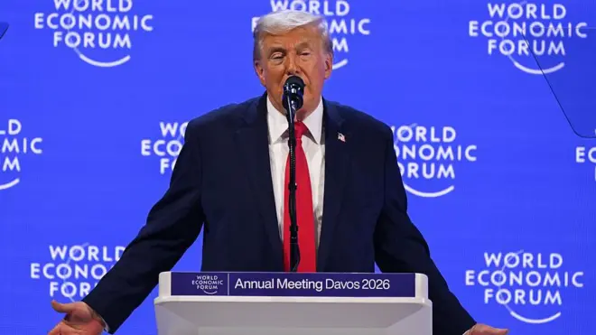 Kırmızı kravatlı lacivert takım elbiseli adam kürsüde konuşuyor. Arkasındaki mavi ekranda World Economic Forum yazıyor. 