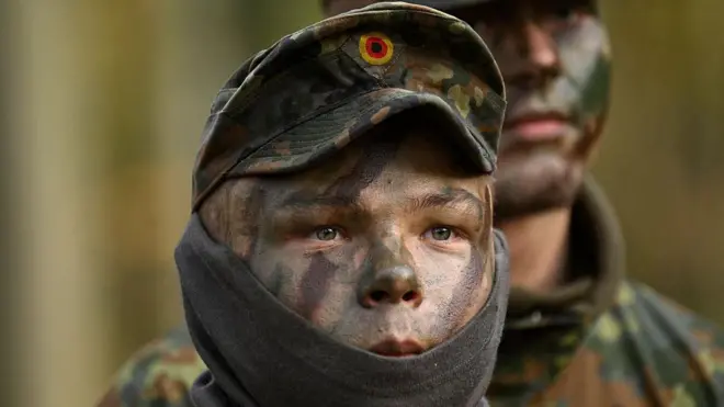 Bir Alman askerin yalnızca burnu ve gözleri görünüyor. Şapka takmış ve yüzüne kamuflaj boyaları sürülü