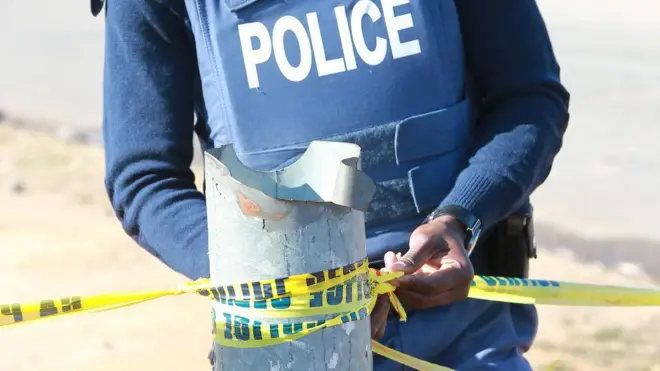 One police man dey hold yellow tape tied to an iron