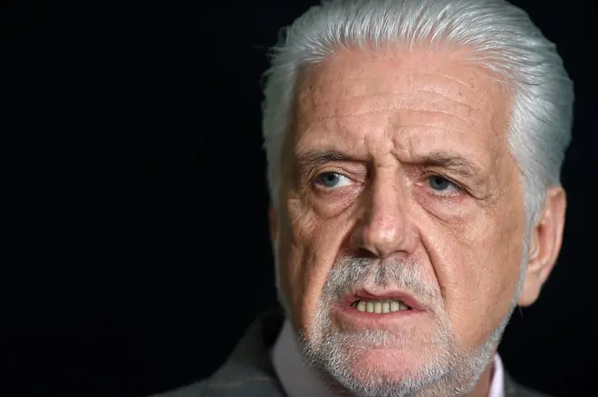 A imagem mostra Jaques Wagner em um retrato fechado, enquadrado dos ombros para cima, com cabelos brancos penteados para trás e barba curta grisalha. Ele olha para o lado, fora da câmera, com expressão séria e concentrada.